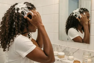 Femme aux cheveux bouclés naturels appliquant une crème coiffante devant son miroir de salle de bain