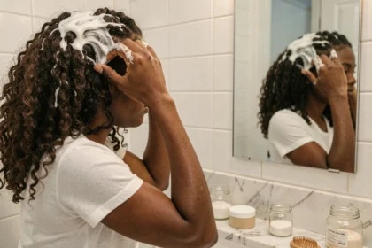 Femme aux cheveux bouclés naturels appliquant une crème coiffante devant son miroir de salle de bain